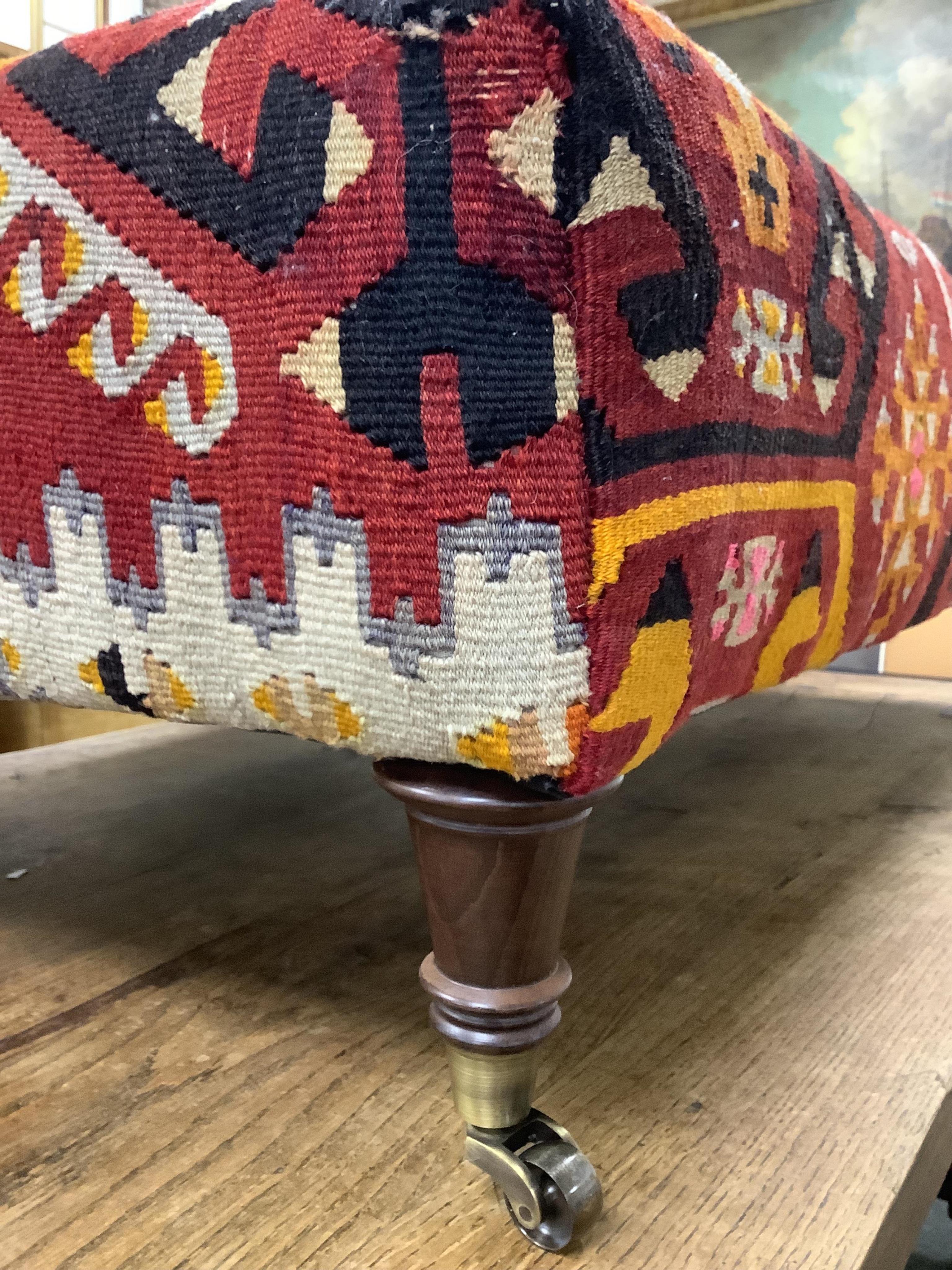 A large contemporary rectangular footstool with antique polychrome Kilim upholstery on turned beech feet with brass caps and castors, width 124cm, depth 78cm, height 40cm.